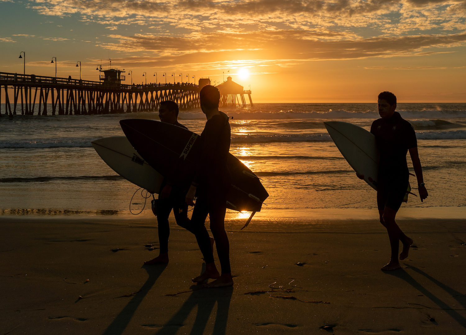 The best surf spots in San Diego featuring Imperial Beach Pier with a surfers walking on the beach at sunset