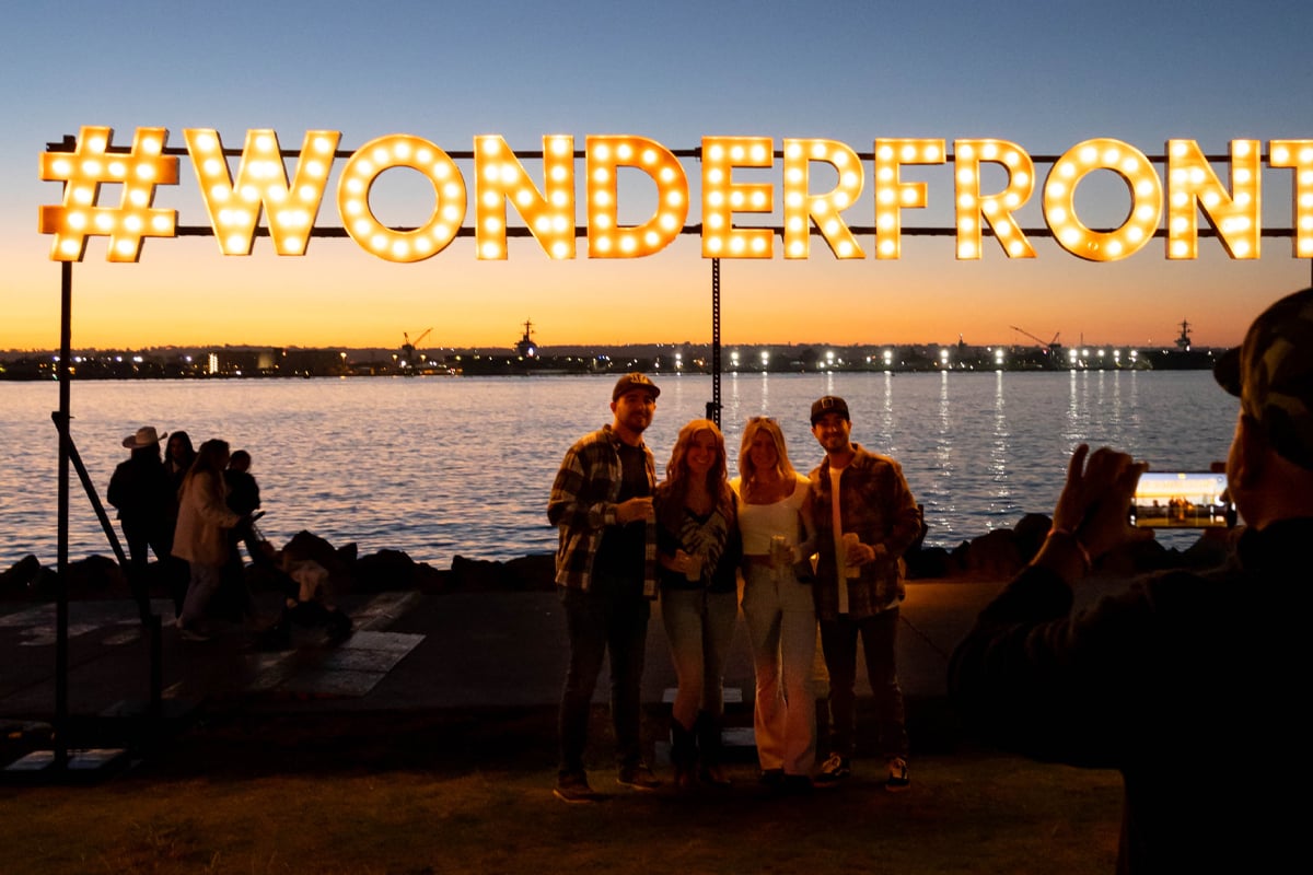 People standing infront of a light sign for the 2024 Wonderfront Music Festival happening this weekend in San Diego May 9-12 at the Embarcadero downtown