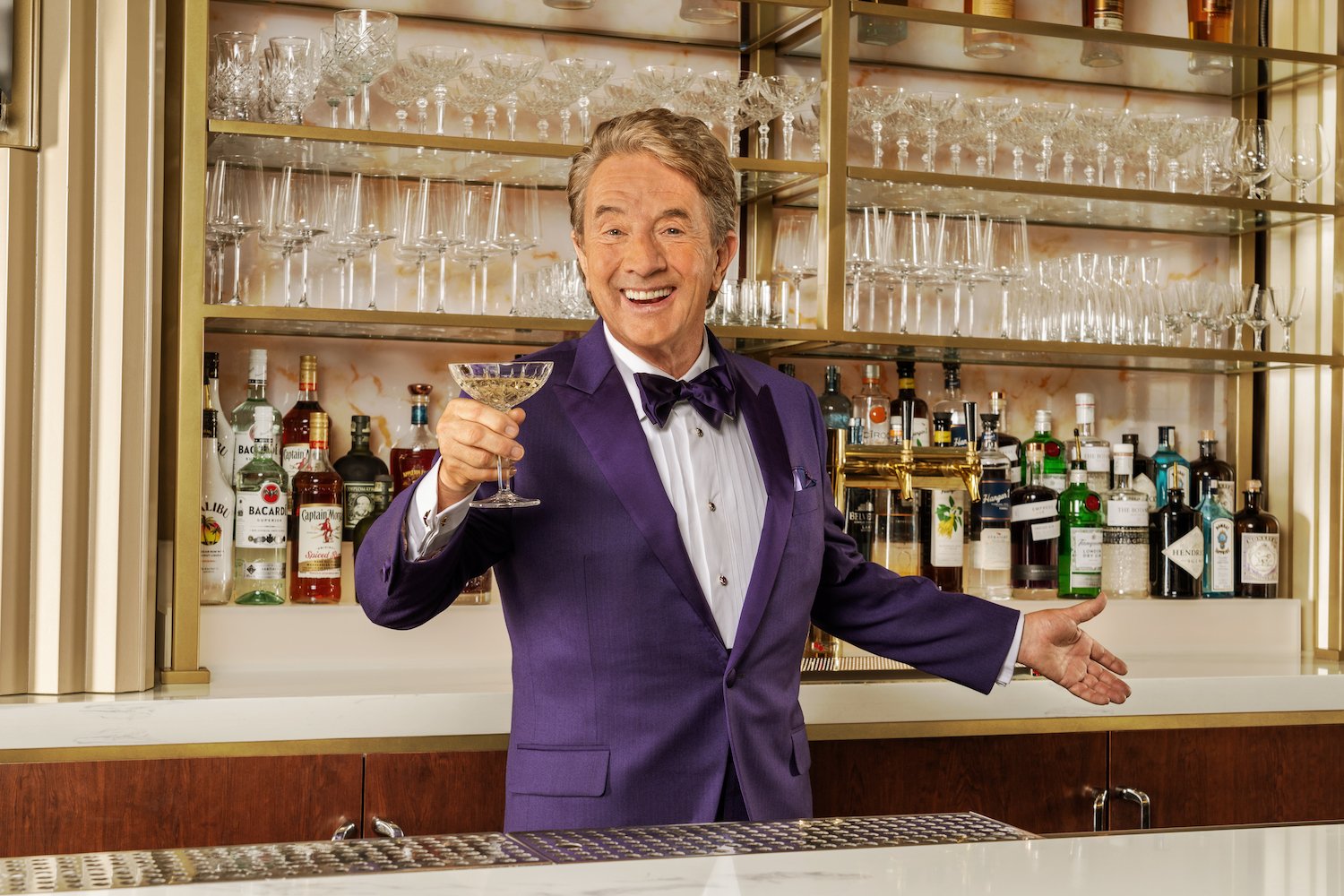 Mayor of Harrah SoCal's Funner, California Martin Short behind a bar holding a martini in a purple suit