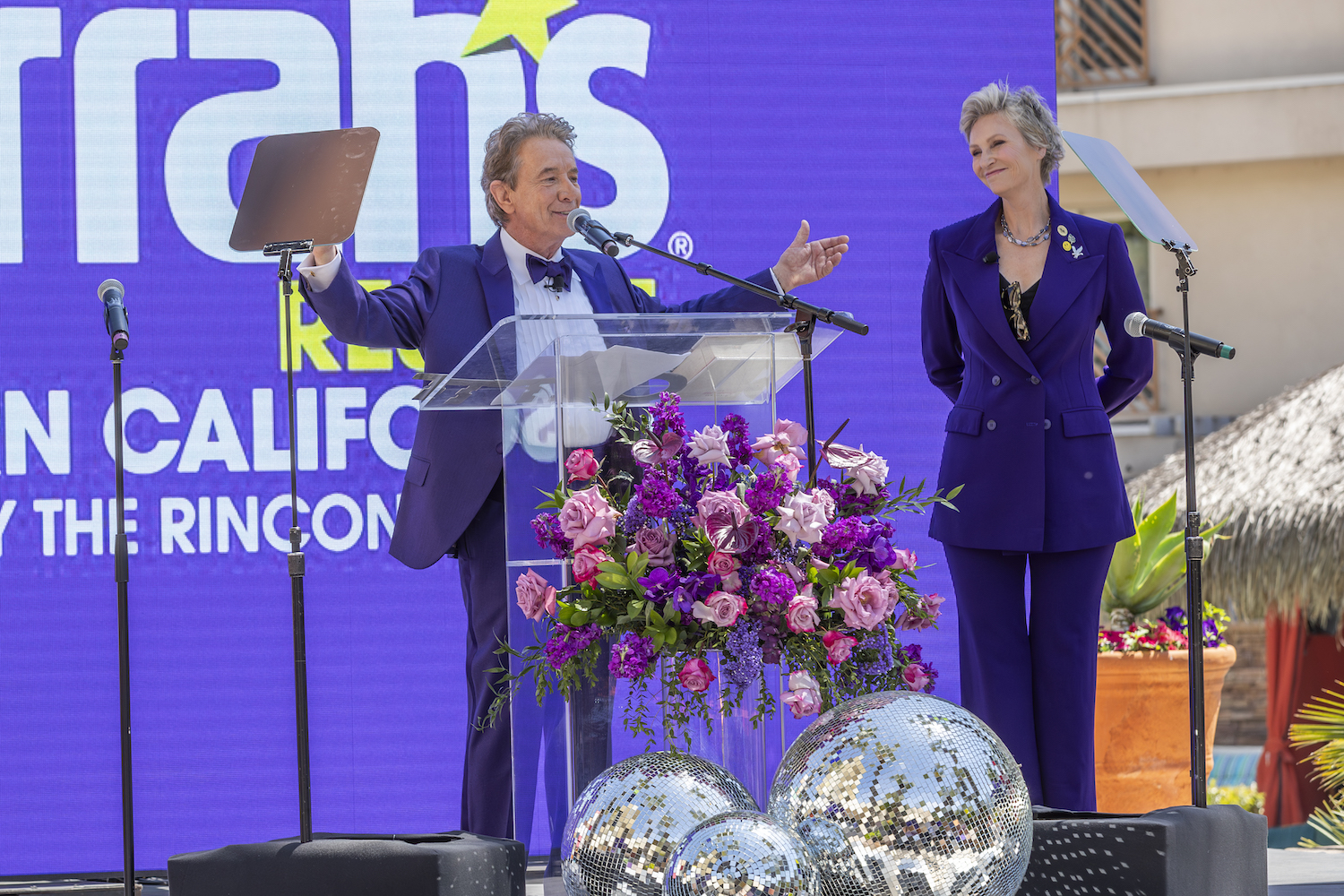 Mayor of Harrah SoCal's Funner, California Martin Short in a purple suit standing with former mayor Jane Lynch
