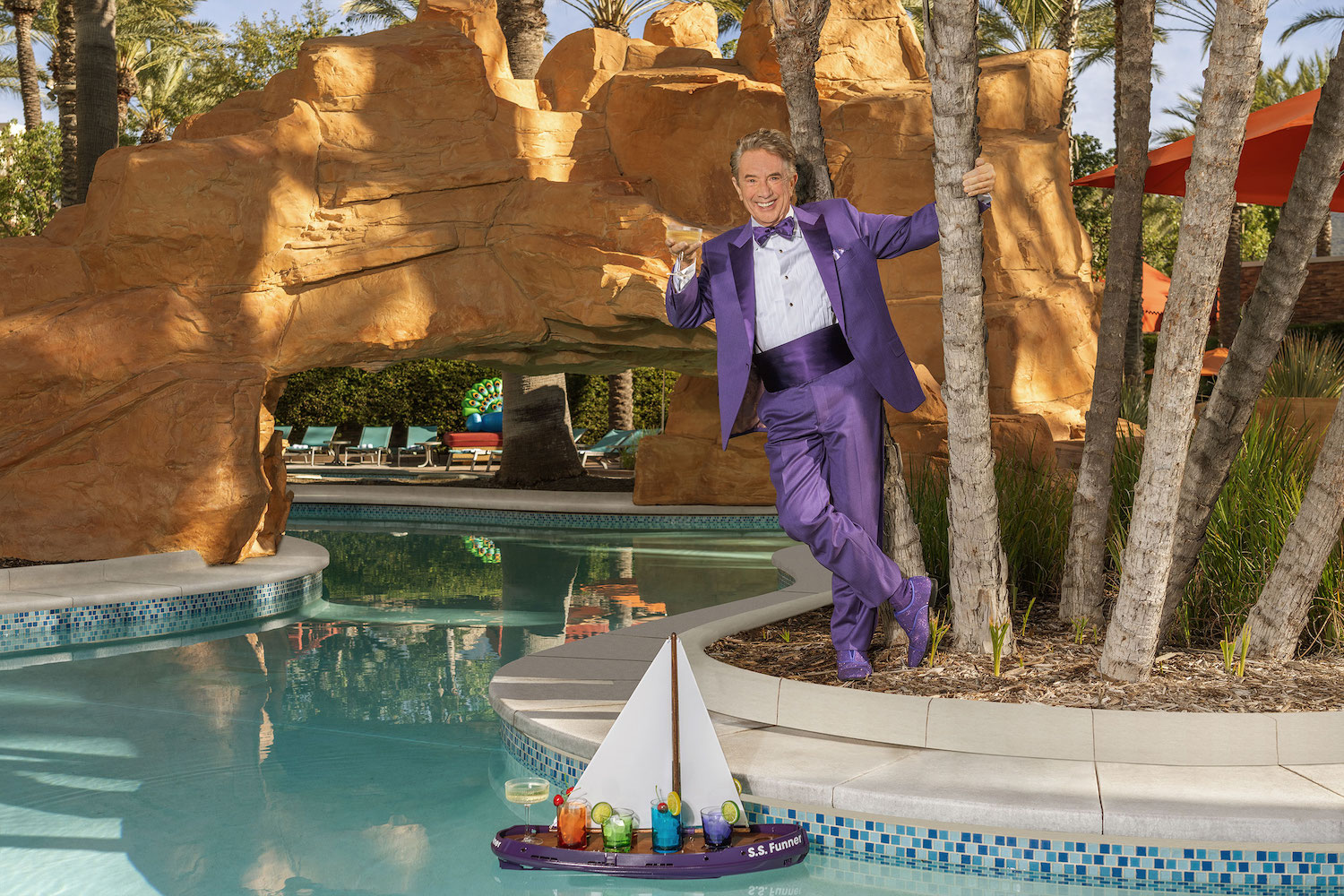 Mayor of Harrah SoCal's Funner, California Martin Short in a purple suit standing by a pool with a cocktail in his hand