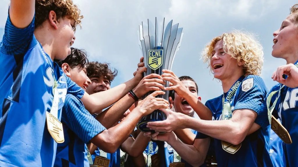 The ECNL Boys Soccer National Playoffs San Diego sports event happening this month featuring soccer players holding a trophy at Surf Sports Park in Del Mar