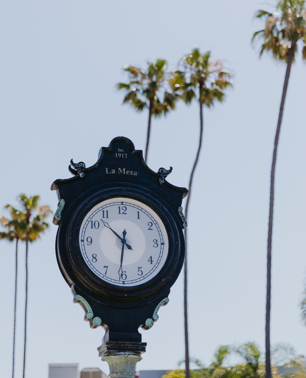 A historic clock in downtown La Mesa, San Diego with palm trees in the background