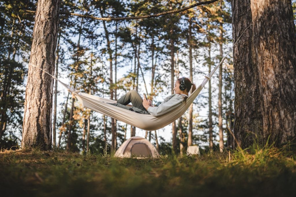 Young woman lying down in a hammock with headphones and use cellphone