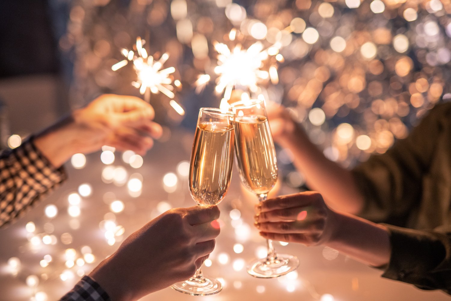 Hands of couple clinking with flutes of champagne and their friends holding sparklers at a San Diego New Years Eve event in 2024