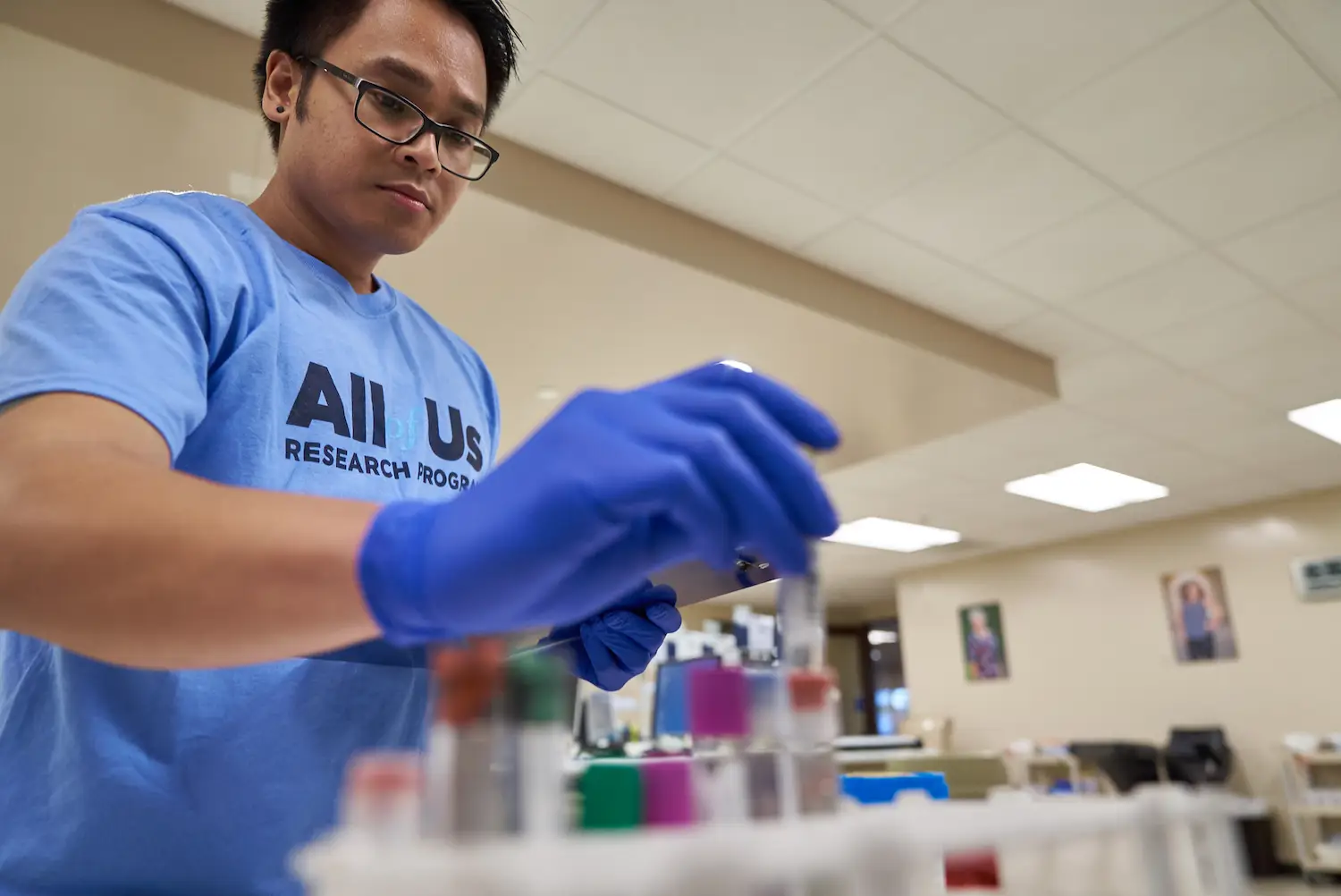 A National Institute of Health researcher in a lab wearing an All of Us Research Program shirt, one of the programs set to be cut by Donald Trump's federal goverment 