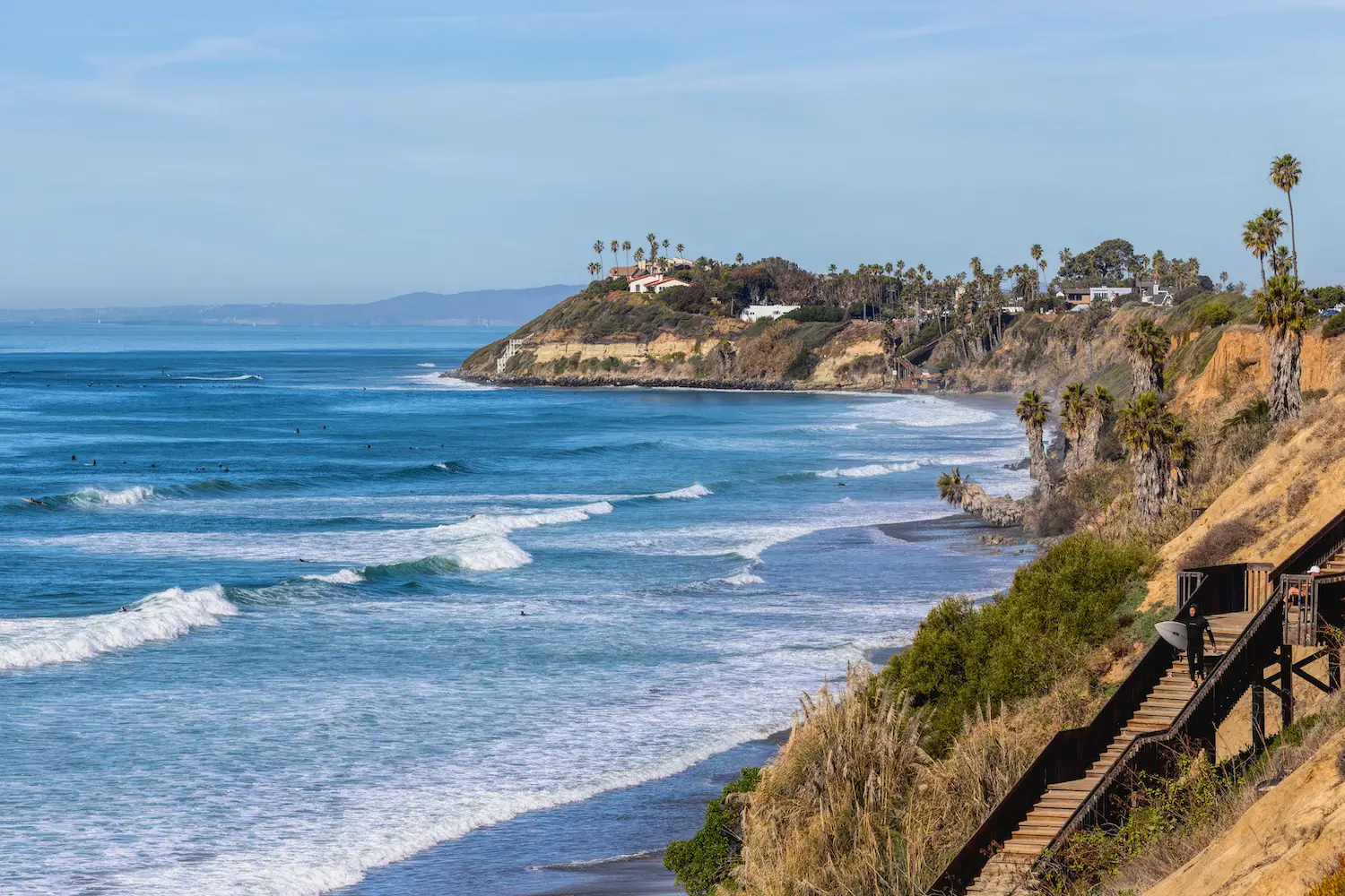 Surfer walking down the stairs at Swamis surf spot in Encinitas, San Diego